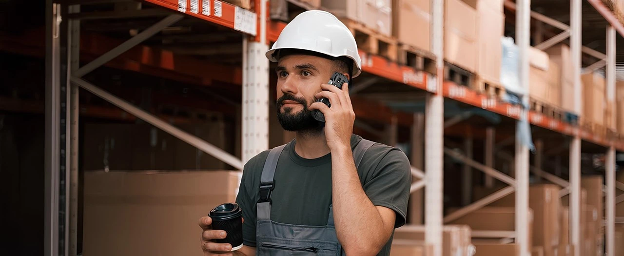 Depo ortamında baretli çalışanın Hammer H Power Plus LTE rugged telefonu ile görüşme yapması